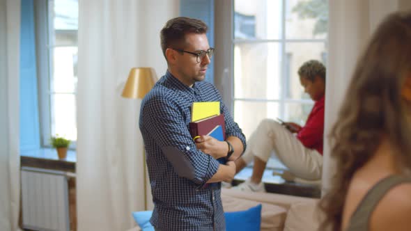 Unconfident Shy Student in Glasses Holding Book Walking in Dorm Common Room