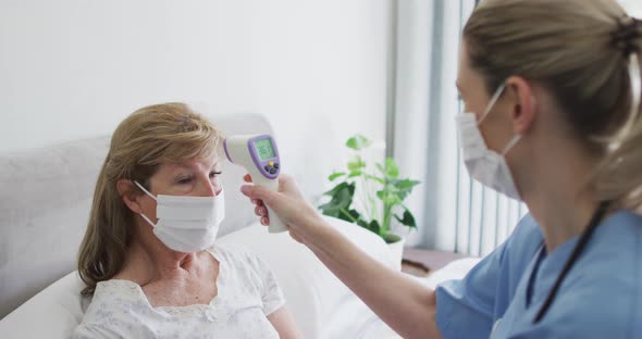 Female health worker checking temperature of senior woman at home