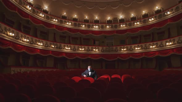 Spectator in mask sitting alone in empty theater. Man putting off his facial mask 