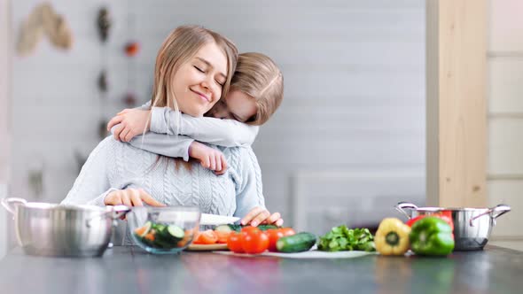 A Cute Girl is Hugging Her Young Mother in a Kitchen