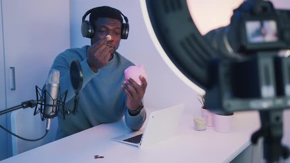 Man Wearing Headphones and Holding a Piggy Bank Recording a Video