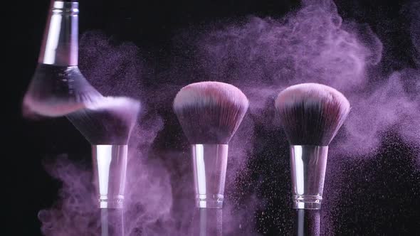 Beauty Concept. Cosmetic Brushes with Pink Cosmetic Powder Spreading on Black Background in Slow