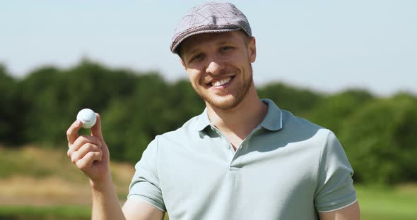 Close Up Outdoor Portrait of Positive Caucasian Male Golf Player Wearing Cap Holding Golf Ball and