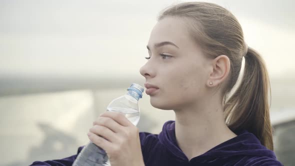 Closeup Face of Confident Slim Beautiful Sportswoman Drinking Refreshing Water Outdoors at the