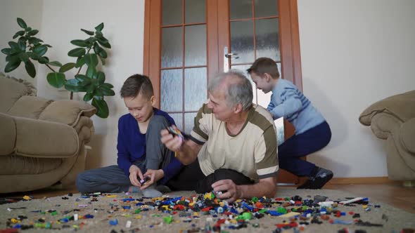 Old man with little boys playing with lots of colorful plastic toys indoor