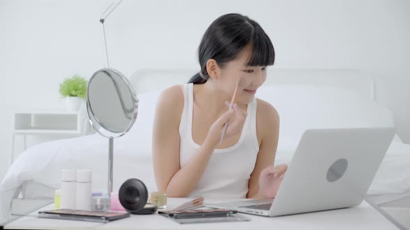 Beauty of young asian woman with learning makeup with brush on cheek on laptop computer.