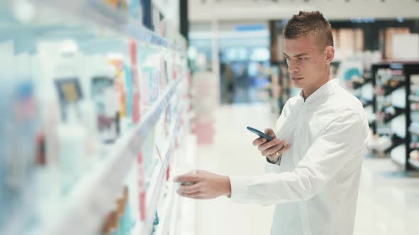 Guy Photographs a Jar with Cosmetics on a Smartphone in a Supermarket