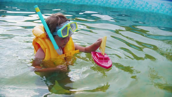 A Little Boy in Underwater Mask Playing with a Toy Boat in the Inflatable Swimming Pool