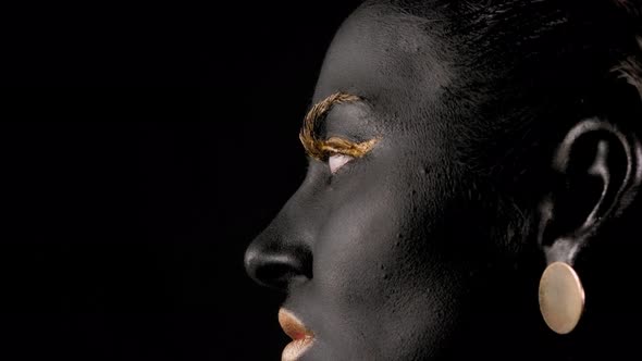 Face of Woman with Black Paint on Her Skin and Golden Lashes She Opens Her Eyes