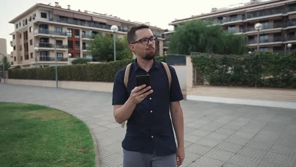 Cheerful Man Is Walking in Square in Summer Day, Looking on Screen of His Mobile