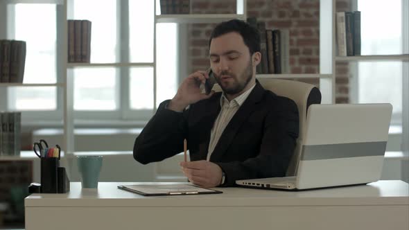 Man Talking on Mobile Phone While Using Laptop Computer