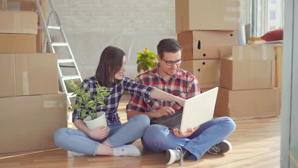 Young Couple with Laptop on the Background of Boxes for Moving