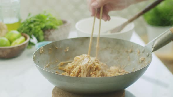 Woman stirring hot wok noodles with chopsticks