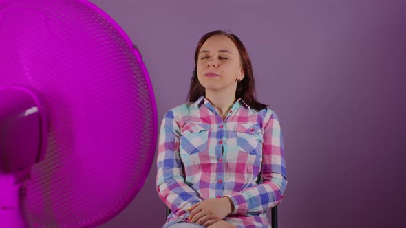 Close Up of Young Woman Sitting on Chair in Front of Fan on Purple Background