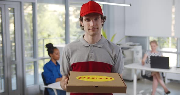 Portrait of Delivery Guy in Uniform Holding Pizza Box Looking at Camera and Talking to Client in