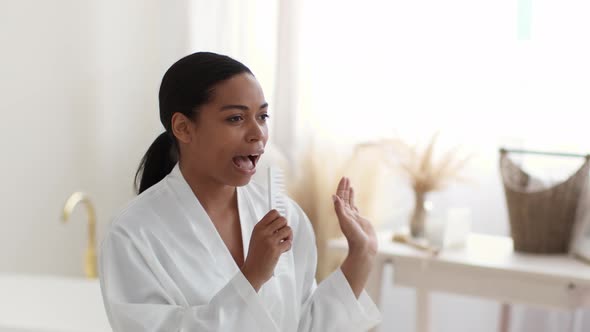 Young Artistic African American Lady Wearing Bathrobe Singing Into Hairbrush Like Mic Performing at