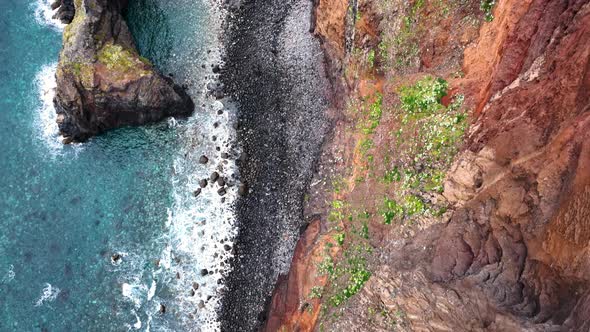 Aerial top-down along black pebble coast and dramatic sea cliffs, azure ocean