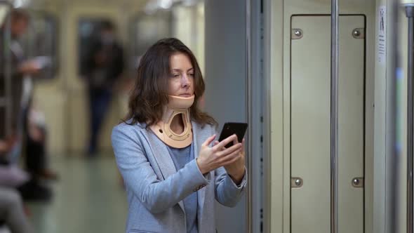 Middle-aged Woman with Neck Pain Is Using Cervical Collar, Traveling By Metro, Using Smartphone in