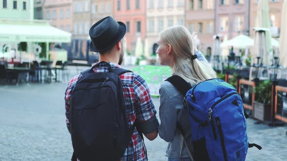 Back View of Tourists Couple with Bags Checking Map on Central City Square