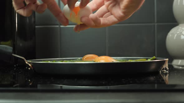 Hand breaking eggs into hot pan