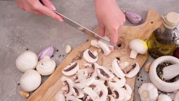 Woman Cuts Champignon Mushrooms with a Knife on a Wooden Cutting Board