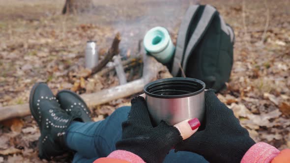 Girl Having Rest with Hot Drink, Tea From Thermos Sitting on the Tree in the Forest.