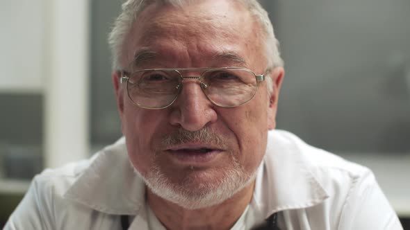 A Grayhaired Doctor with Glasses Speaks in Closeup and Shows a Confident Gesture with His Hands Slow