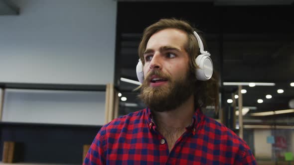 Caucasian businessman walking wearing headphones dancing in a modern office