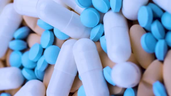 Vertical Video White Capsules Lie on Bright Orange Tablets with Small Blue Painkillers