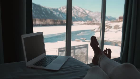 A Woman Lies on a Bed Next to a Laptop and Looks Out the Window