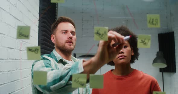 A Young Man and Woman are Planning in the Office Drawing on a Glass Board