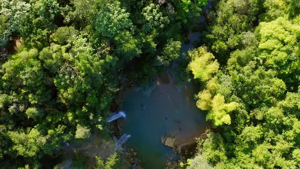 Waterfall plunges into freshwater pool in middle of jungle; drone top down