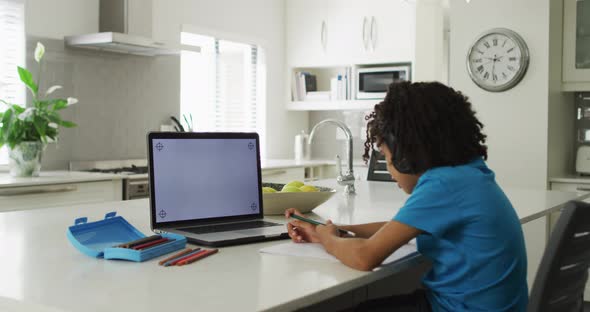 Happy biracial boy sitting at table using laptop with copy space and having online classes