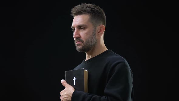 Sad Parishioner Holding Bible Closing Eyes on Dark Background, Holy Scripture