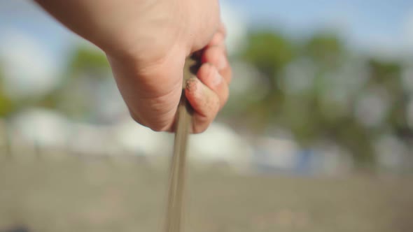 close-up hand grabs a handful of dry sand and lets it fall between his fingers