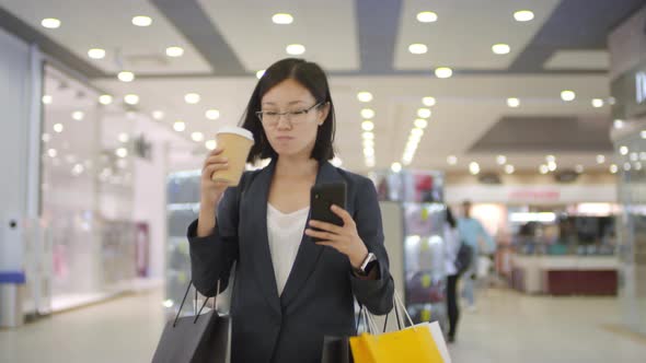 Stylish Chinese Shopper Walking through Mall with Coffee and Smartphone