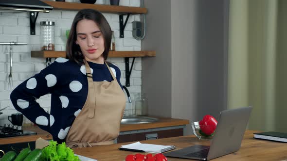Tired woman writes culinary recipe in notebook massages neck after using laptop