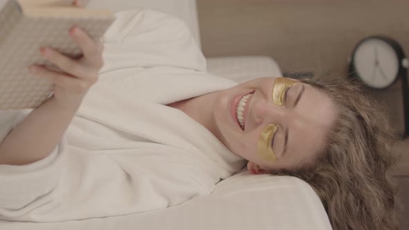 Smiling Young Woman with Eye Patches Reading Book in Bed