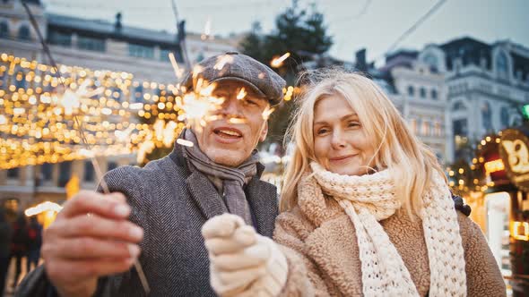 Happy Senior Spouses Walking Outdoor Together Enjoying Sparkling Bengal Lights on City Square
