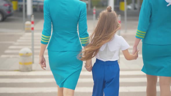 Back View of Little Girl Walking To Airport Gates Holding Hands of Stewardesses. Professional