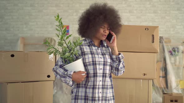 African Woman with an Afro Hairstyle with a Plant in His Hand Talking on the Phone Next To the Boxes