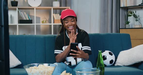 African American Woman in Sportswear Sitting on the Couch at Home and Talking on Phone