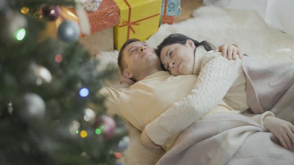 Hugging Happy Smiling Couple Lying on Soft Carpet at Christmas Tree and New Year Presents