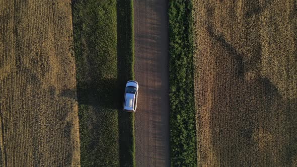 Aerial zenith view of silver car parked on dirt road then heading off while camera is following from
