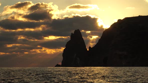 A Red Burning Sunset with the Silhouette of a Cliff Over the Sea