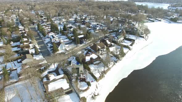 Aerial drone over snow-covered houses residential area on a riverbank