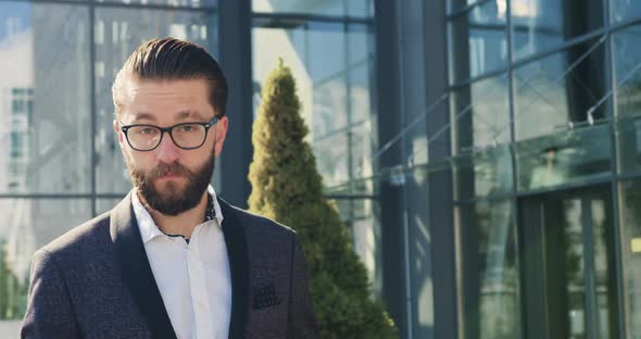 Businessman in Glasses which Poses on Camera Near Modern Glass Building During Time Break for Coffee