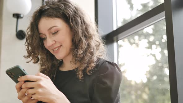 Woman Looks Into Smartphone Laughs Reading News By Window