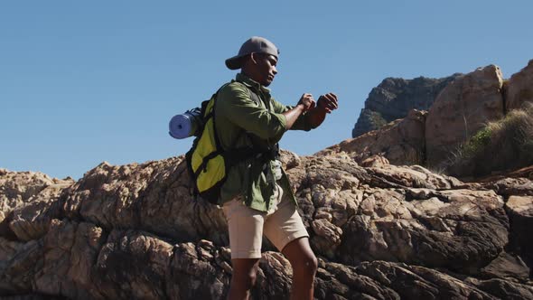 African american man hiking in countryside by the coast using his smartwatch