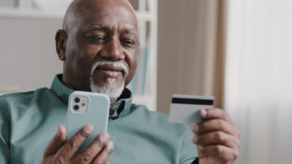 Elderly African Dominican Old Mature Man at Home Online Transaction Buying Hold Smartphone Credit